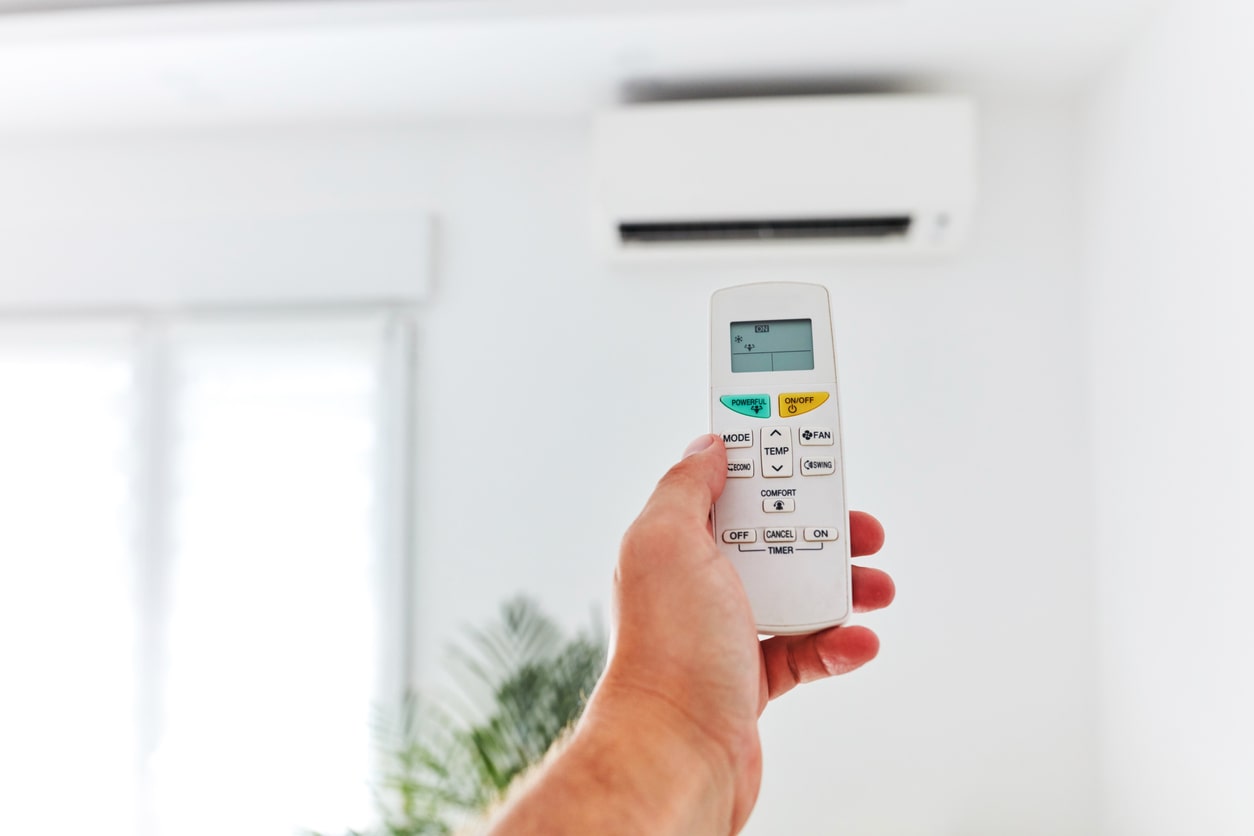 A hand pointing an AC remote control at a ductless mini-split system.