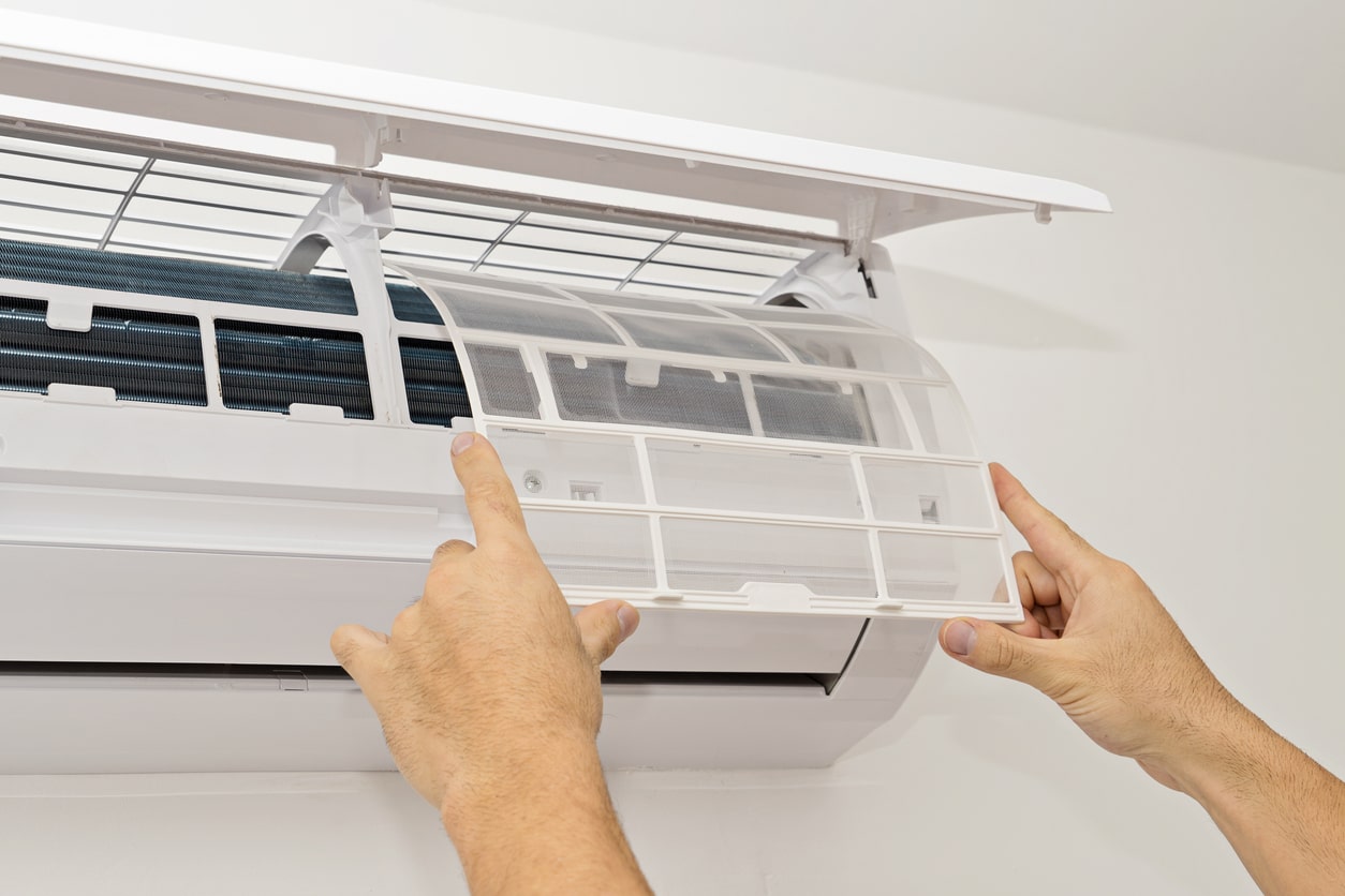 A person's hands shown changing the air filters on a mini-split AC system.