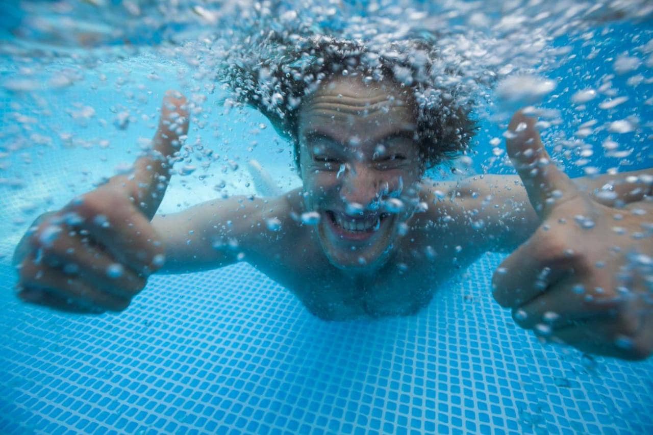 A man underwater in a swimming pool giving two thumbs up.
